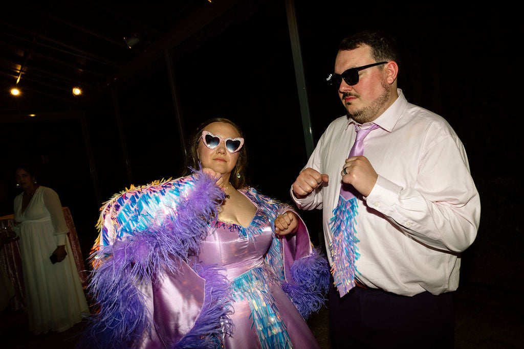 Chandler and Bryan against a dark background wearing sunglasses and posing in their wedding outfits